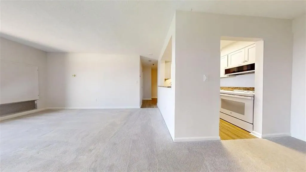 Kitchen with electric stove, light colored carpet, light countertops, and white cabinets