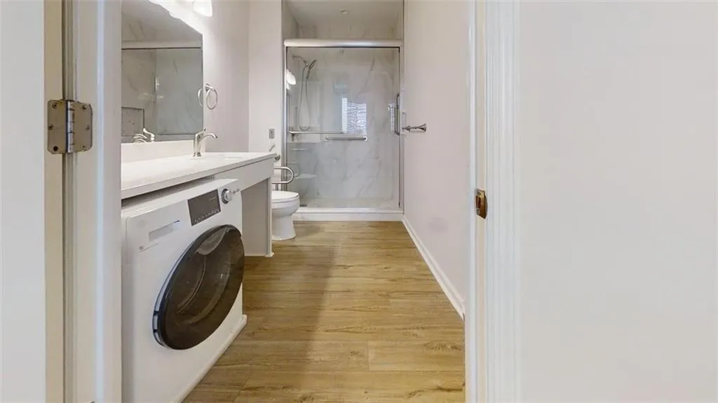 Bathroom featuring washer / dryer, vanity, a marble finish shower, and light wood-style floors