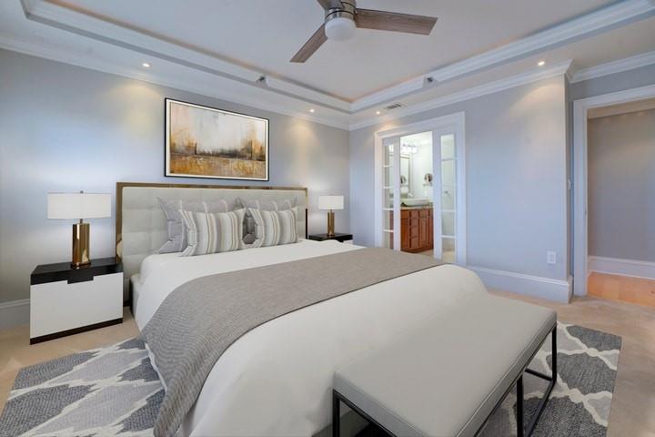 Carpeted bedroom with a raised ceiling, connected bathroom, ceiling fan, and ornamental molding