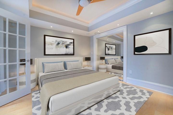 Bedroom featuring light hardwood / wood-style flooring, ceiling fan, and a raised ceiling