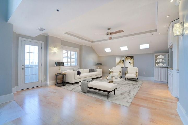 Living room featuring light hardwood / wood-style flooring, ceiling fan, and a tray ceiling