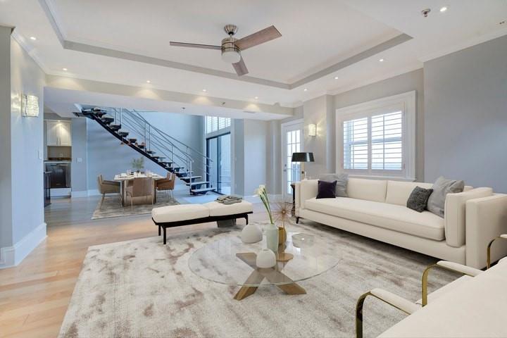 Living room featuring light hardwood / wood-style flooring, ceiling fan, a tray ceiling, and ornamental molding