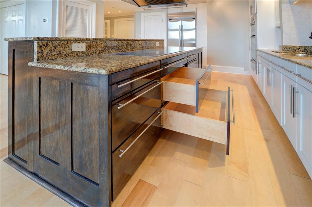 Kitchen with high quality fridge, a kitchen island, light stone counters, dark brown cabinets, and white cabinets