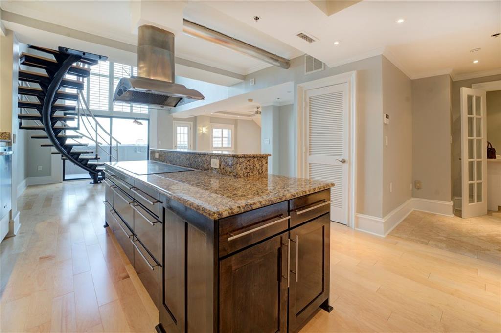 Kitchen with dark brown cabinetry, black electric stovetop, light stone counters, island range hood, and a center island