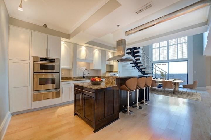 Kitchen with light hardwood / wood-style flooring, light stone counters, a kitchen bar, white cabinetry, and wall chimney exhaust hood