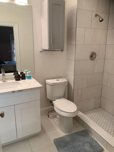 Bathroom featuring tile patterned flooring, toilet, a tile shower, and vanity