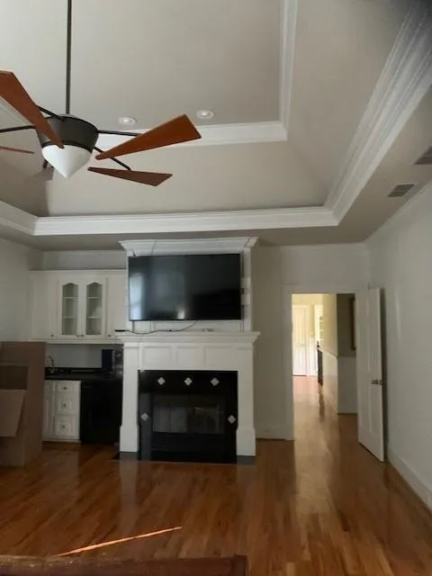Unfurnished living room with ceiling fan, a raised ceiling, hardwood / wood-style floors, and crown molding