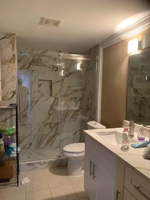 Bathroom featuring tile patterned flooring, toilet, a shower with door, and vanity