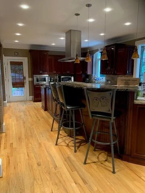 Kitchen featuring decorative light fixtures, island exhaust hood, a kitchen bar, and light hardwood / wood-style flooring