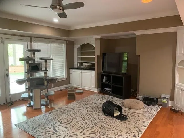 Living room featuring hardwood / wood-style floors, ornamental molding, ceiling fan, and built in features