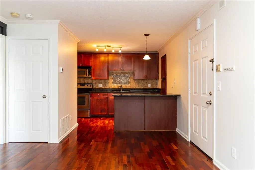 Kitchen featuring dark wood-style floors, stainless steel appliances, backsplash, dark countertops, and a peninsula