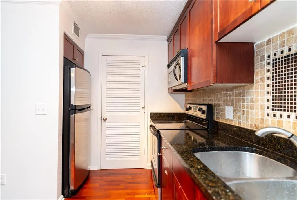 Kitchen with a sink, decorative backsplash, stainless steel appliances, visible vents, and dark wood-style floors