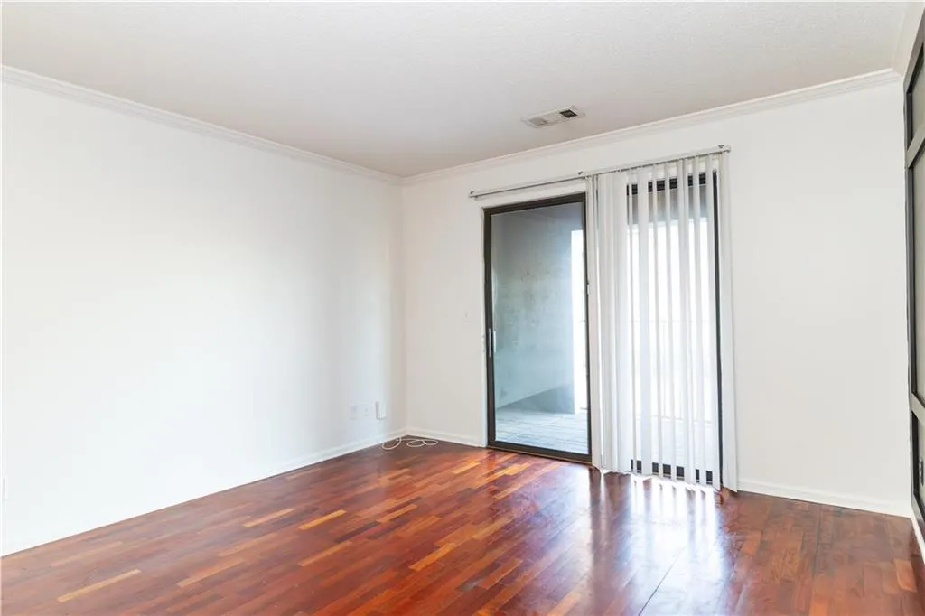 Empty room with dark wood-style flooring, crown molding, visible vents, and baseboards