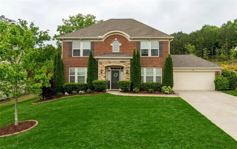 Traditional brick exterior with stone accents, mature landscaping, a two-car garage, and a concrete driveway