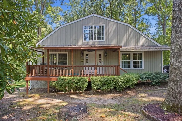Front exterior with a covered porch, wood-tone decking, vertical siding, and mature trees