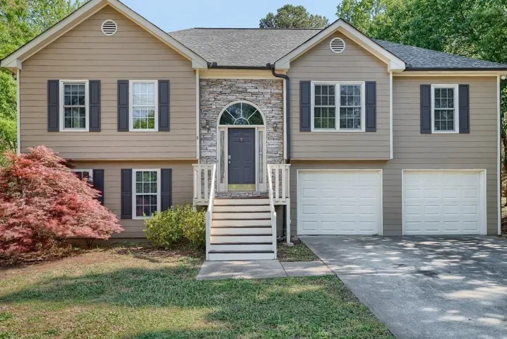 Split-level residence featuring a stone facade entry, a pair of two-car garages, and a paved driveway