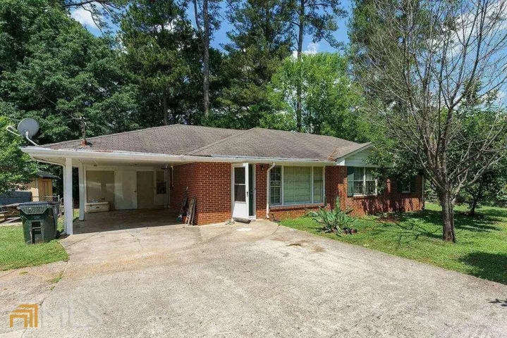 Brick exterior with a covered carport, concrete driveway, and mature landscaping