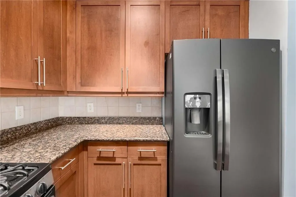 Kitchen with appliances with stainless steel finishes, light stone countertops, brown cabinets, and decorative backsplash