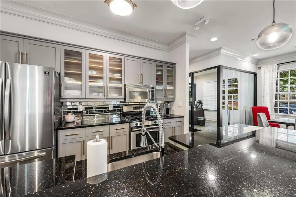 Kitchen featuring gray cabinets, appliances with stainless steel finishes, dark stone countertops, glass insert cabinets, and tasteful backsplash