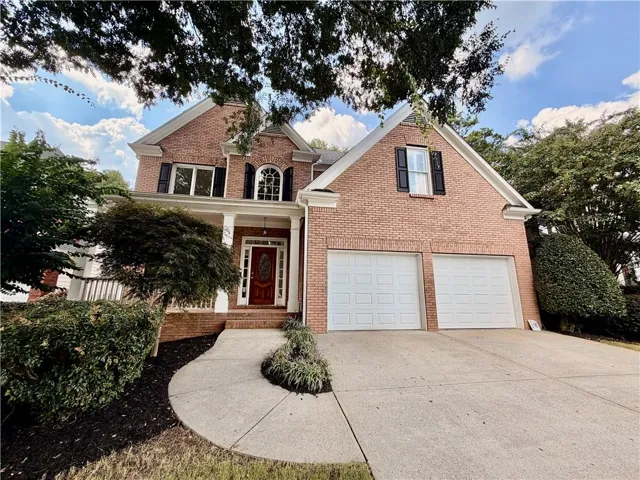 Brick exterior featuring a covered porch with white columns, a red front door, and a two-car garage