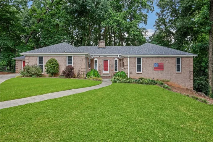 Brick exterior residence featuring a curved walkway, verdant lawn, mature trees, and a prominent red front door