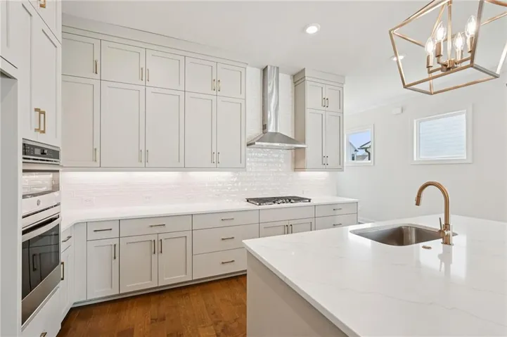 Contemporary kitchen featuring light-toned cabinetry with brass hardware, quartz countertops, a subway tile backsplash, stainless steel appliances, and wood-finish flooring