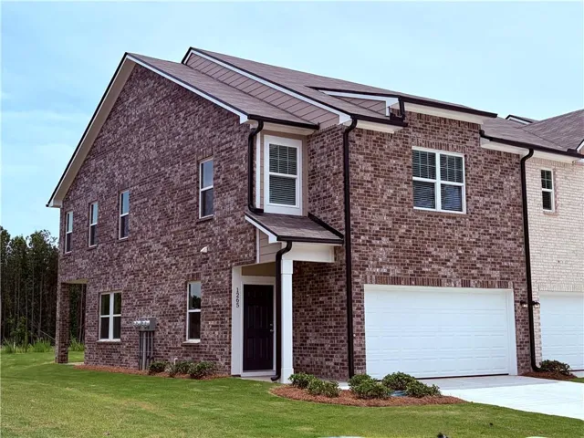 Brick exterior with white window frames, a dark entry door, and an attached garage with a white door