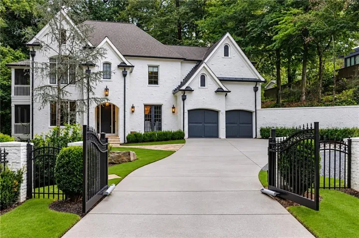 White brick exterior with dark trim windows, integrated two-car garage, gated driveway, and mature landscaping