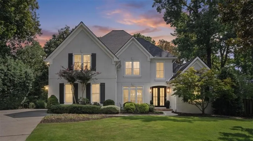 Stucco exterior with a dark shingle roof, featuring multiple gables, black window shutters, and a double-door entryway