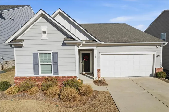Single-story residence featuring light gray siding with brick accents, an attached garage, a paved driveway, and a covered entry