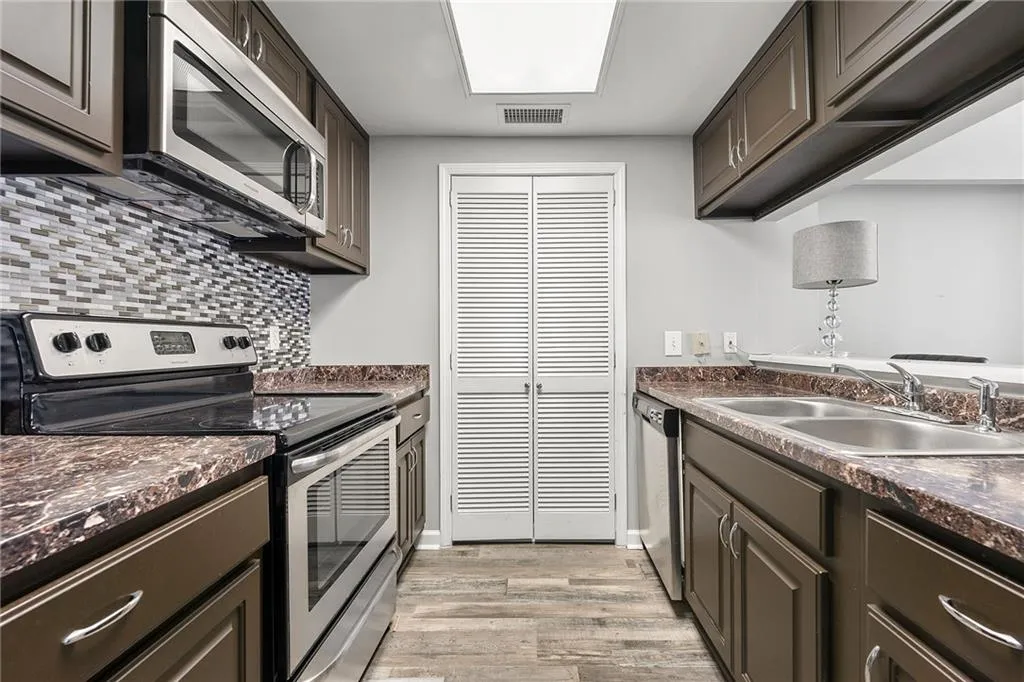 Kitchen with appliances with stainless steel finishes, dark countertops, light wood finished floors, and decorative backsplash