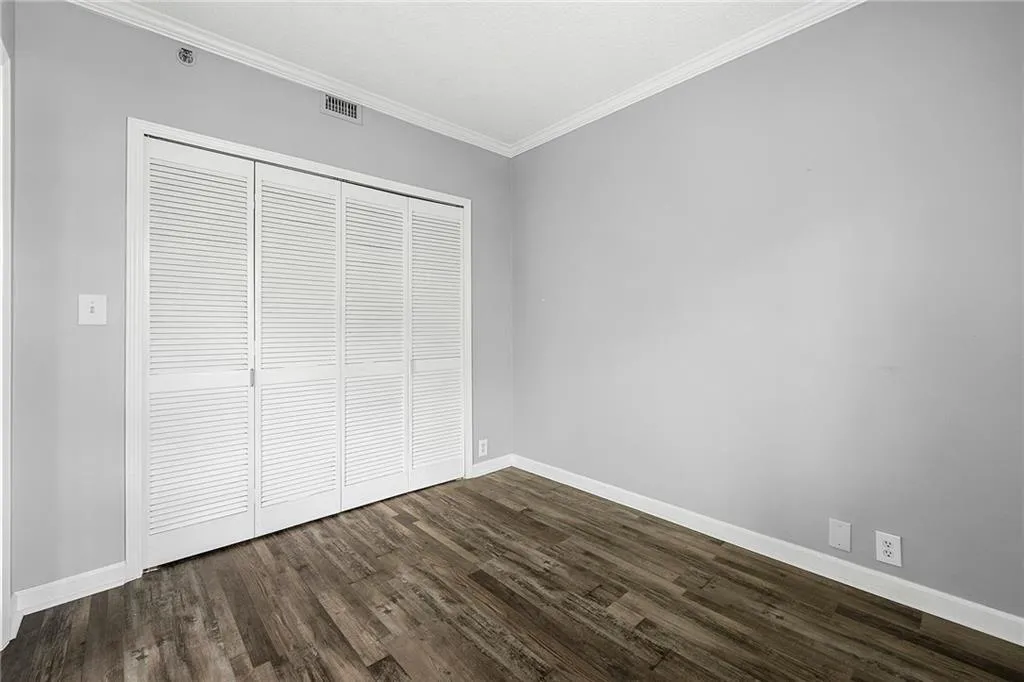 Unfurnished bedroom featuring dark wood-type flooring, crown molding, and a closet