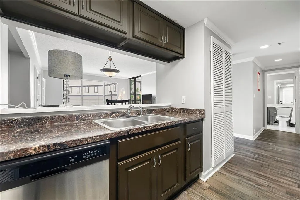 Kitchen featuring dishwasher, dark countertops, dark wood-style flooring, dark brown cabinetry, and crown molding