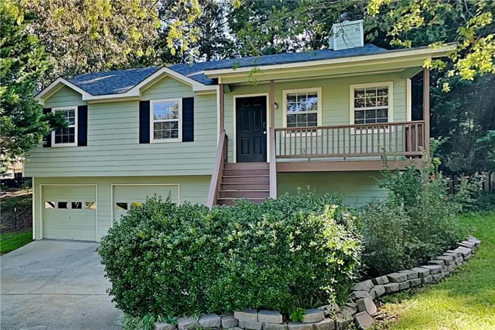Split-level exterior featuring light green siding, dark front door, front balcony with railing, concrete driveway, and two-car garage