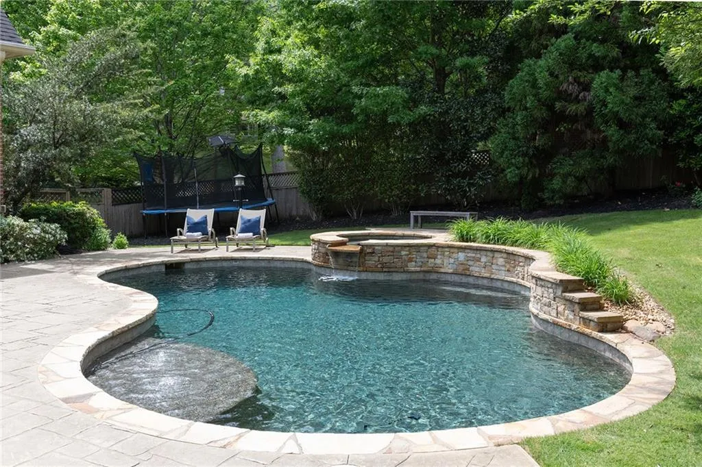 View of swimming pool featuring a trampoline, a yard, and an in ground hot tub