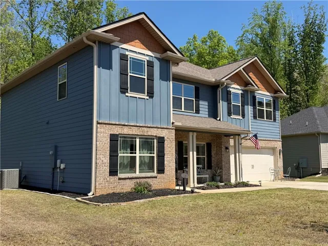 Two-story residence featuring a brick and blue siding exterior, a covered front porch, and a two-car garage
