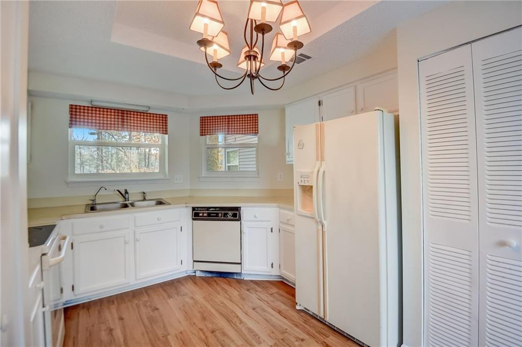 Kitchen featuring an inviting chandelier, white appliances, light hardwood / wood-style flooring, sink, and white cabinetry