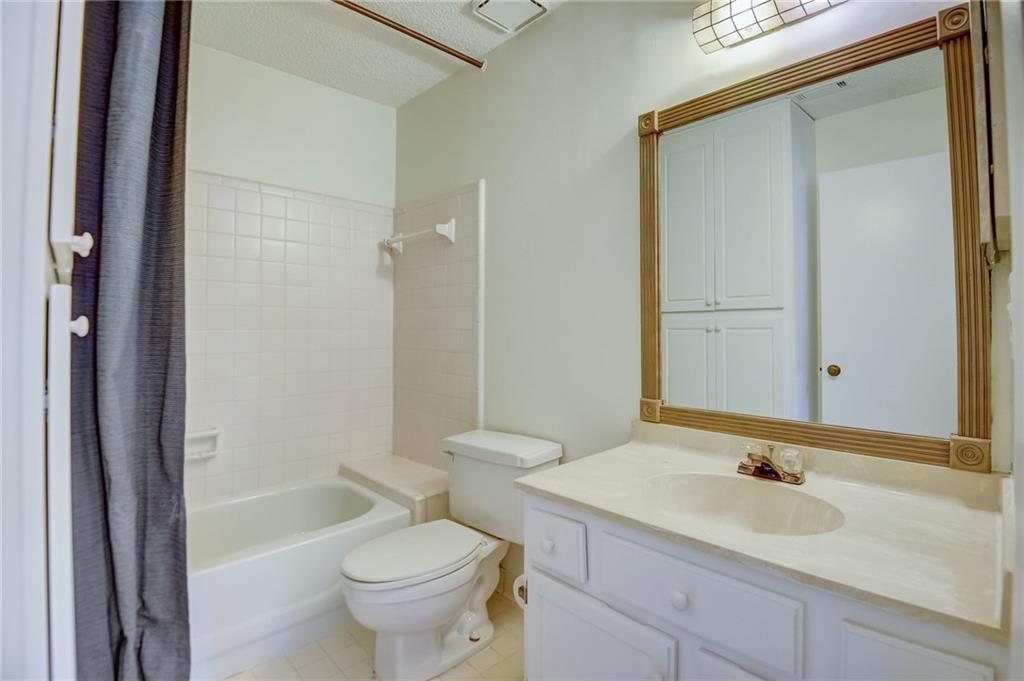 Full bathroom with a textured ceiling, toilet, shower / bath combination with curtain, vanity with extensive cabinet space, and tile flooring
