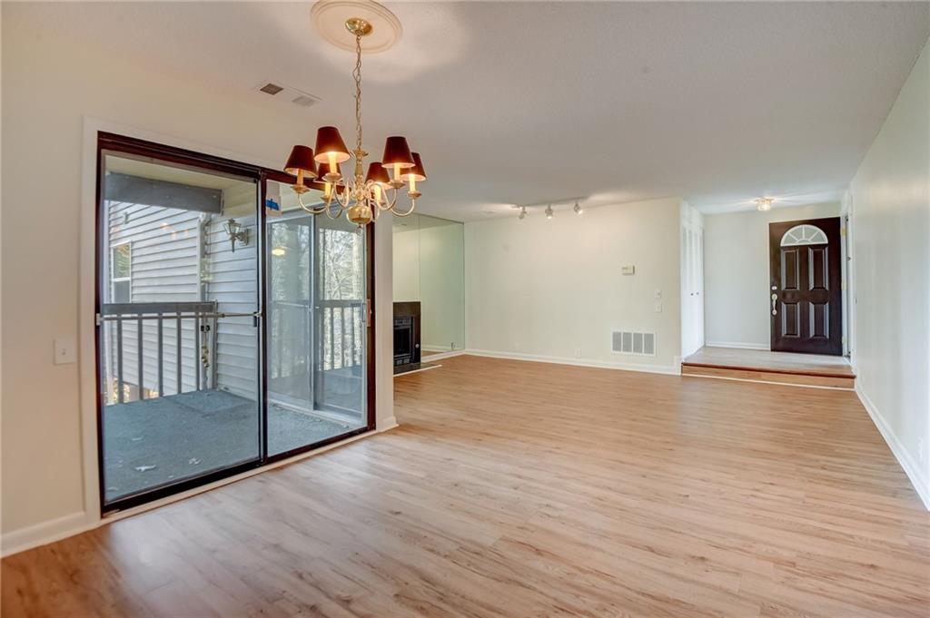 Empty room with light wood-type flooring, a notable chandelier, and track lighting