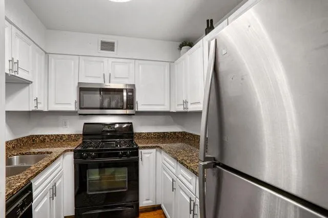 Kitchen with black appliances, white cabinetry, and dark stone counters