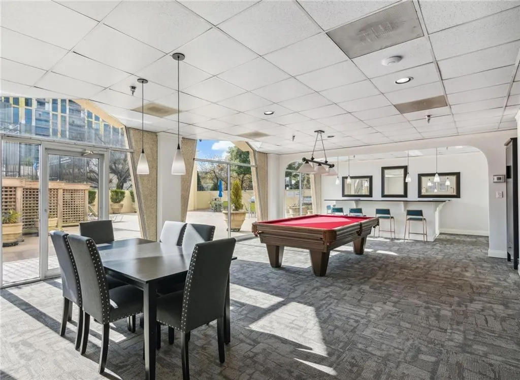 Recreation room with a paneled ceiling, billiards table, carpet, a wall of windows, and arched walkways