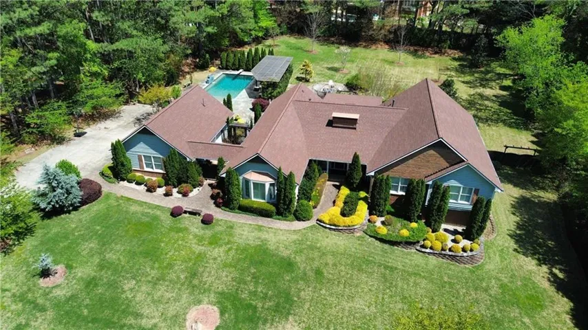 Expansive property featuring a large swimming pool, paved patio, mature trees, and landscaped grounds