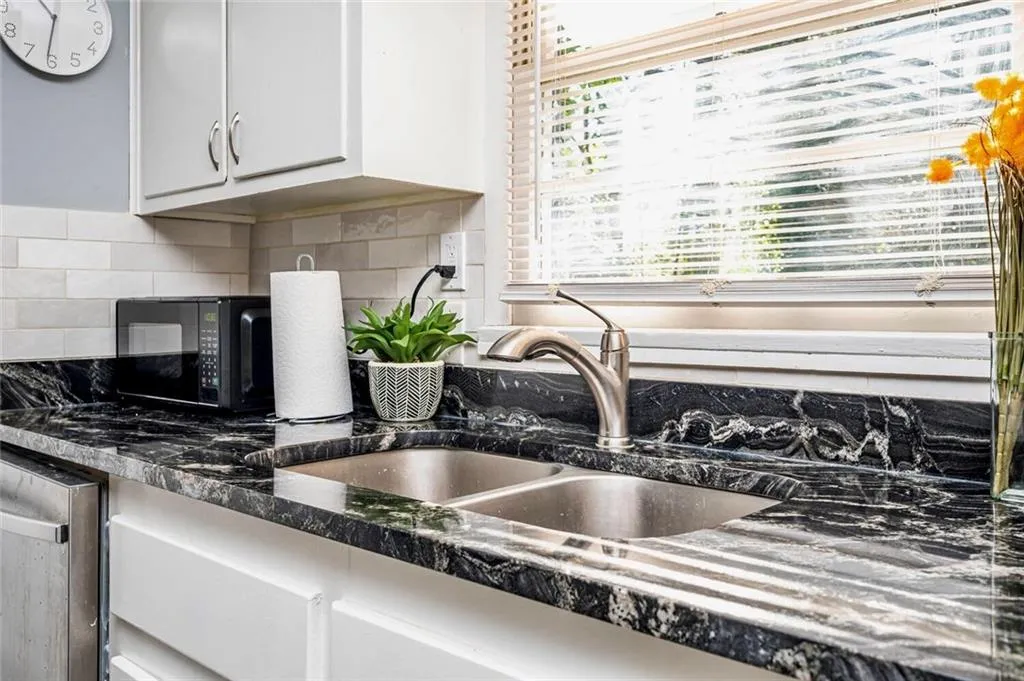 Kitchen view of decorative backsplash, stainless steel dishwasher, black microwave, dark stone counters, and white cabinetry