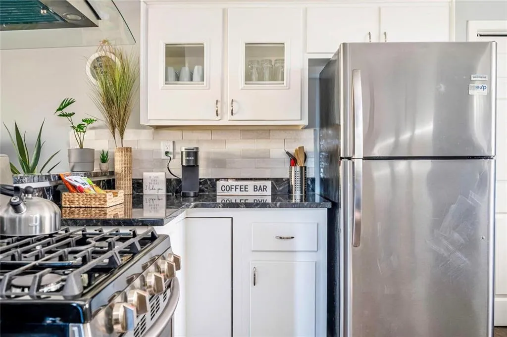 Kitchen with appliances with stainless steel finishes, white cabinets, tasteful backsplash, glass insert cabinets, and range hood