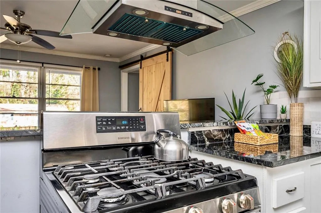Kitchen with crown molding, stainless steel gas stove, a barn door, extractor fan, and dark stone counters