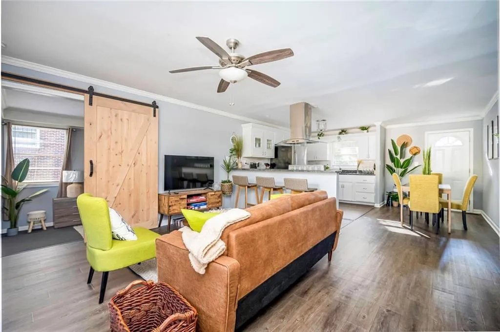 Living area with ornamental molding, ceiling fan, dark wood finished floors, and a barn door