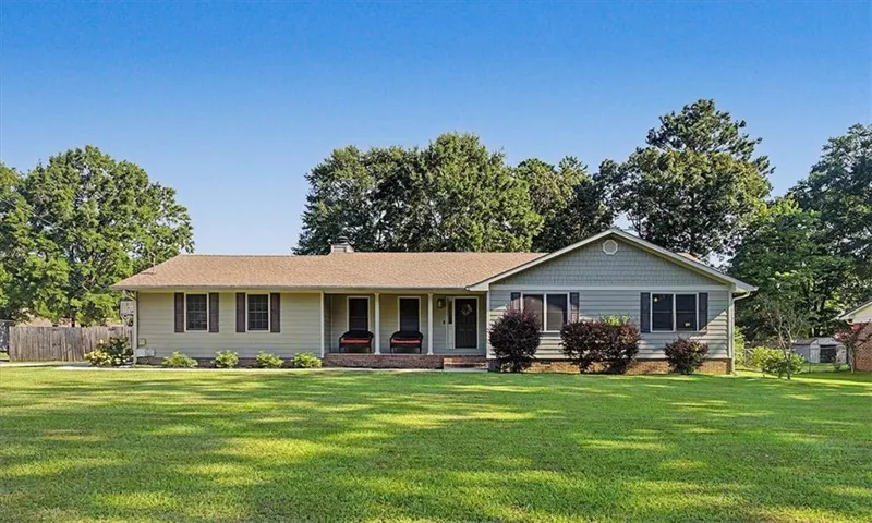 Ranch-style residence featuring a covered front porch, light-toned siding, and brown window shutters