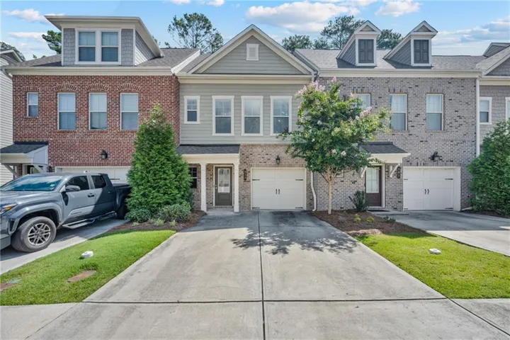 Multi-level townhome featuring a mix of brick and siding exteriors, multiple dormer windows, individual garage doors, and private entryways