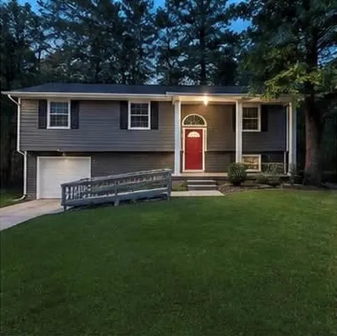 Split-level residence featuring gray siding, a bright red entry door with an arched transom, a single-car garage, and a front yard