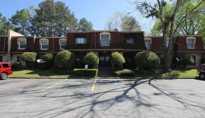 Solid brick exterior with symmetrical facade and multiple windows, complemented by manicured landscaping featuring mature shrubs and trees